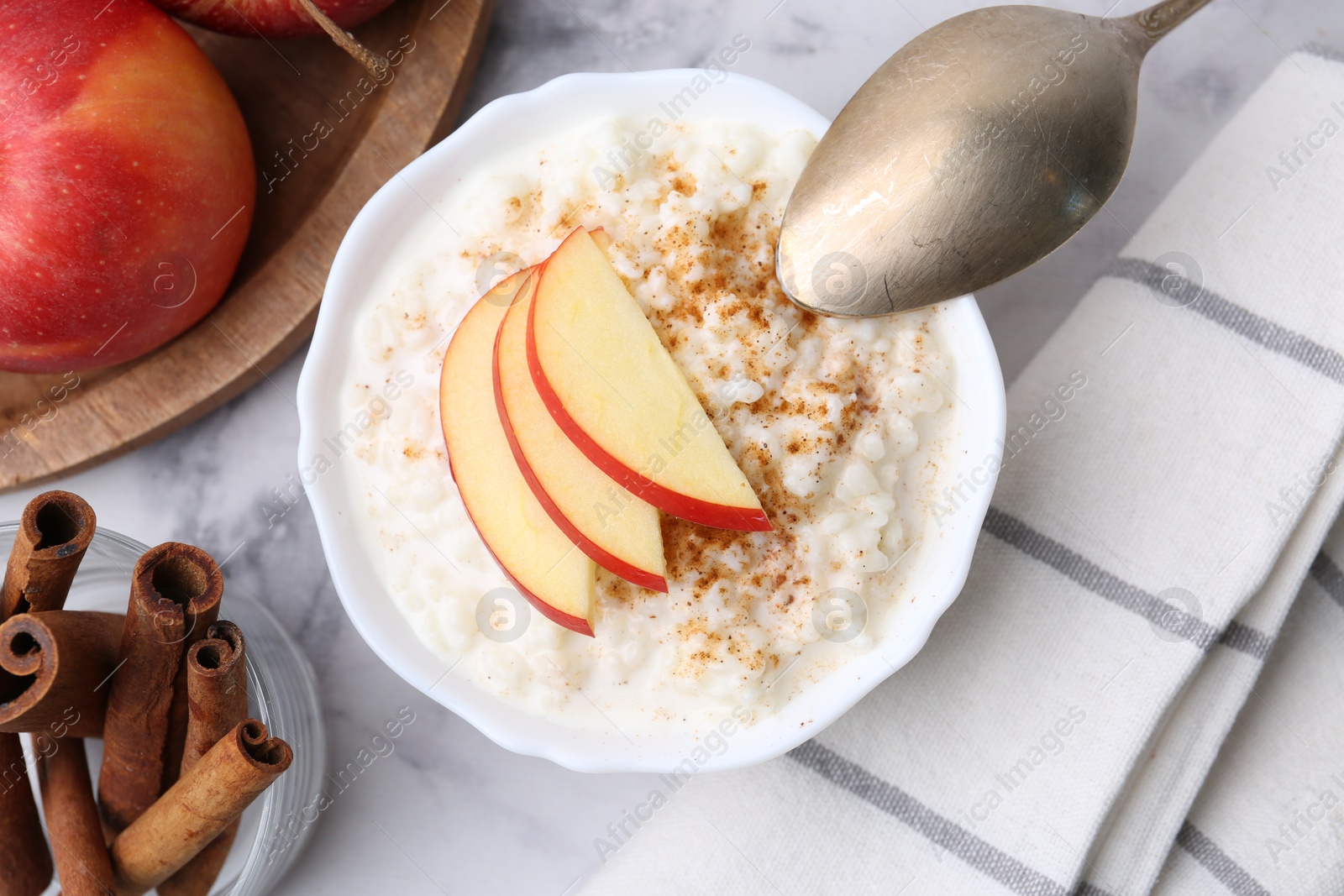 Photo of Delicious rice pudding with cinnamon and apples on white marble table, flat lay