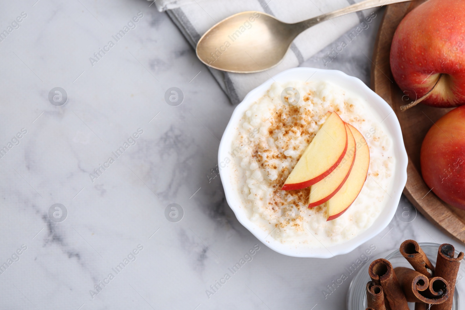 Photo of Delicious rice pudding with cinnamon and apples on white marble table, flat lay. Space for text