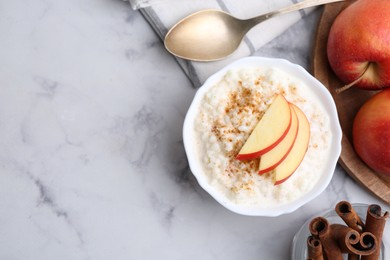 Photo of Delicious rice pudding with cinnamon and apples on white marble table, flat lay. Space for text