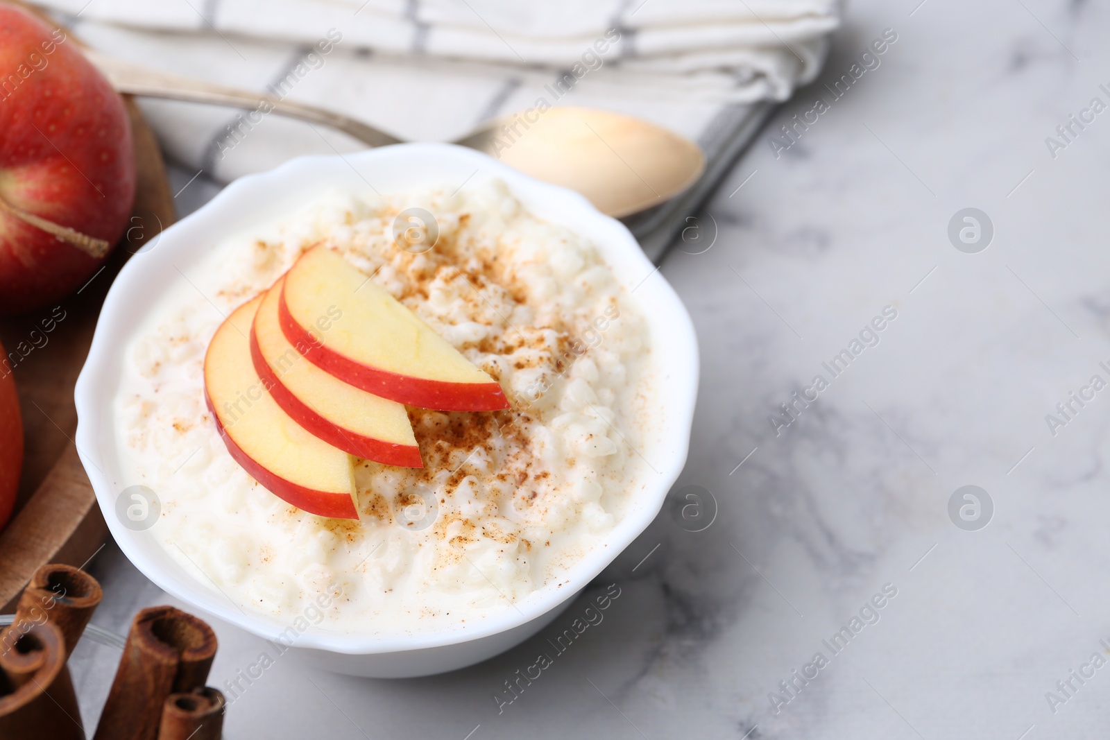 Photo of Delicious rice pudding with cinnamon and apples on white marble table, closeup. Space for text