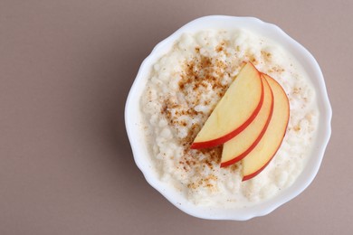 Photo of Delicious rice pudding with cinnamon and apple on dark beige background, top view. Space for text