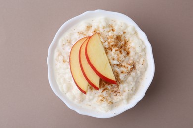 Photo of Delicious rice pudding with cinnamon and apple on dark beige background, top view