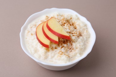 Photo of Delicious rice pudding with cinnamon and apple on dark beige background, closeup