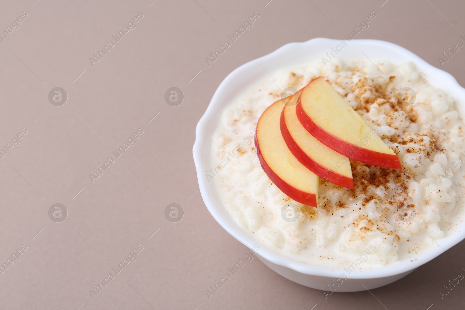 Photo of Delicious rice pudding with cinnamon and apple on dark beige background, closeup. Space for text