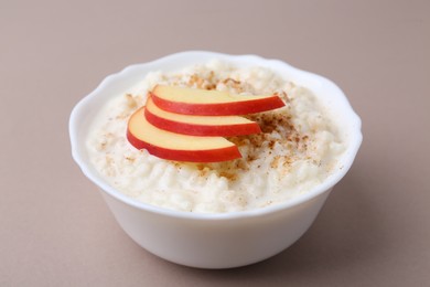 Photo of Delicious rice pudding with cinnamon and apple on dark beige background, closeup