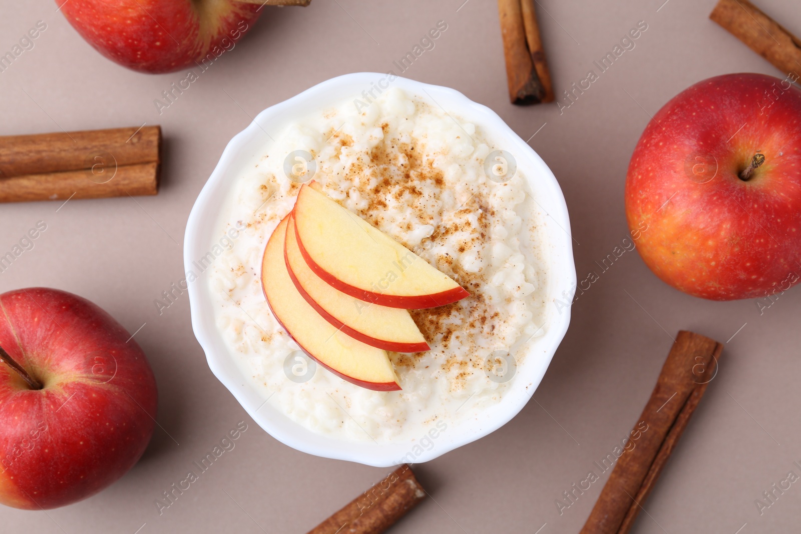 Photo of Delicious rice pudding with apples and cinnamon sticks on dark beige background, flat lay