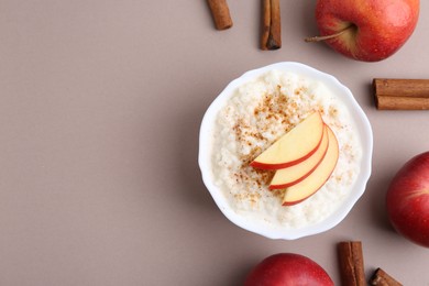 Photo of Delicious rice pudding with apples and cinnamon sticks on dark beige background, flat lay. Space for text