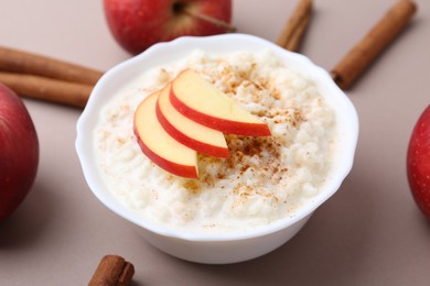 Photo of Delicious rice pudding with apples and cinnamon sticks on dark beige background, closeup