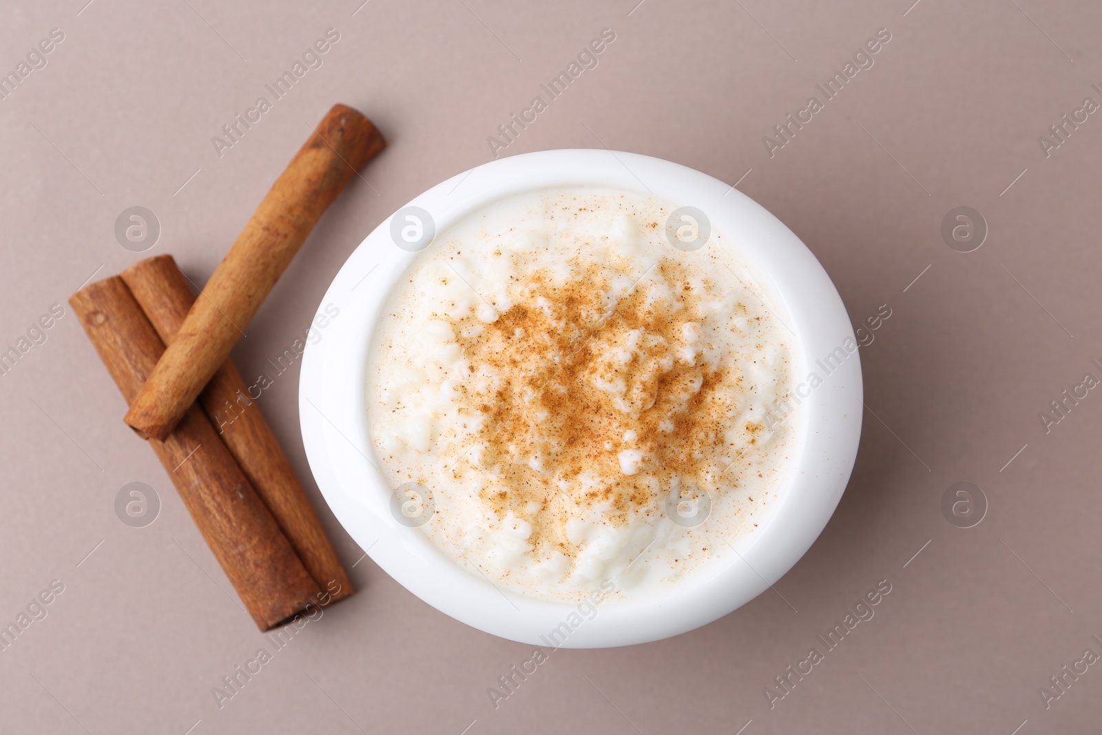 Photo of Delicious rice pudding with cinnamon sticks on dark beige background, top view