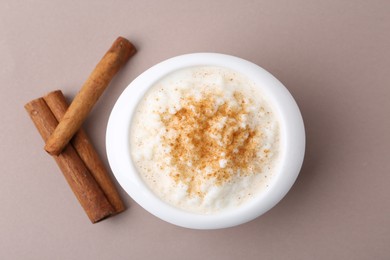 Photo of Delicious rice pudding with cinnamon sticks on dark beige background, top view