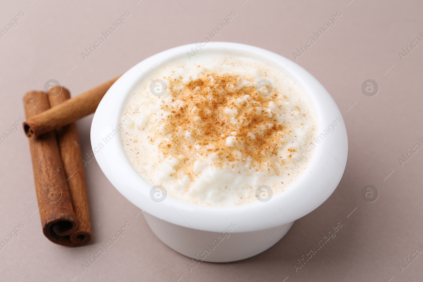 Photo of Delicious rice pudding with cinnamon sticks on dark beige background, closeup