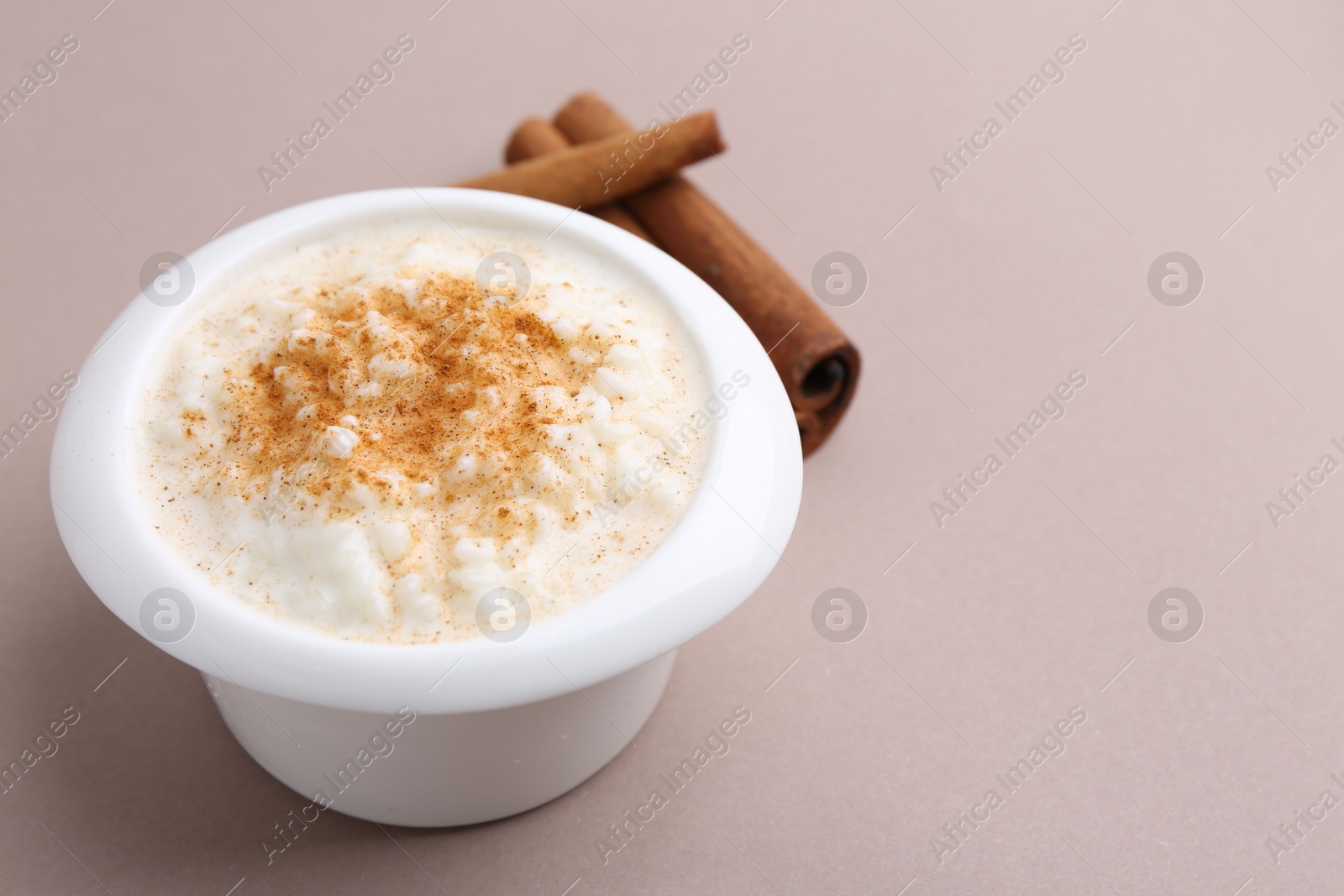 Photo of Delicious rice pudding with cinnamon sticks on dark beige background, closeup. Space for text