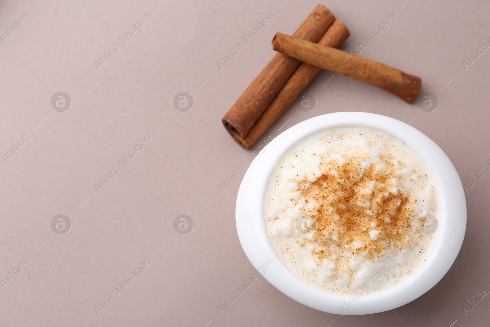 Photo of Delicious rice pudding with cinnamon sticks on dark beige background, top view. Space for text