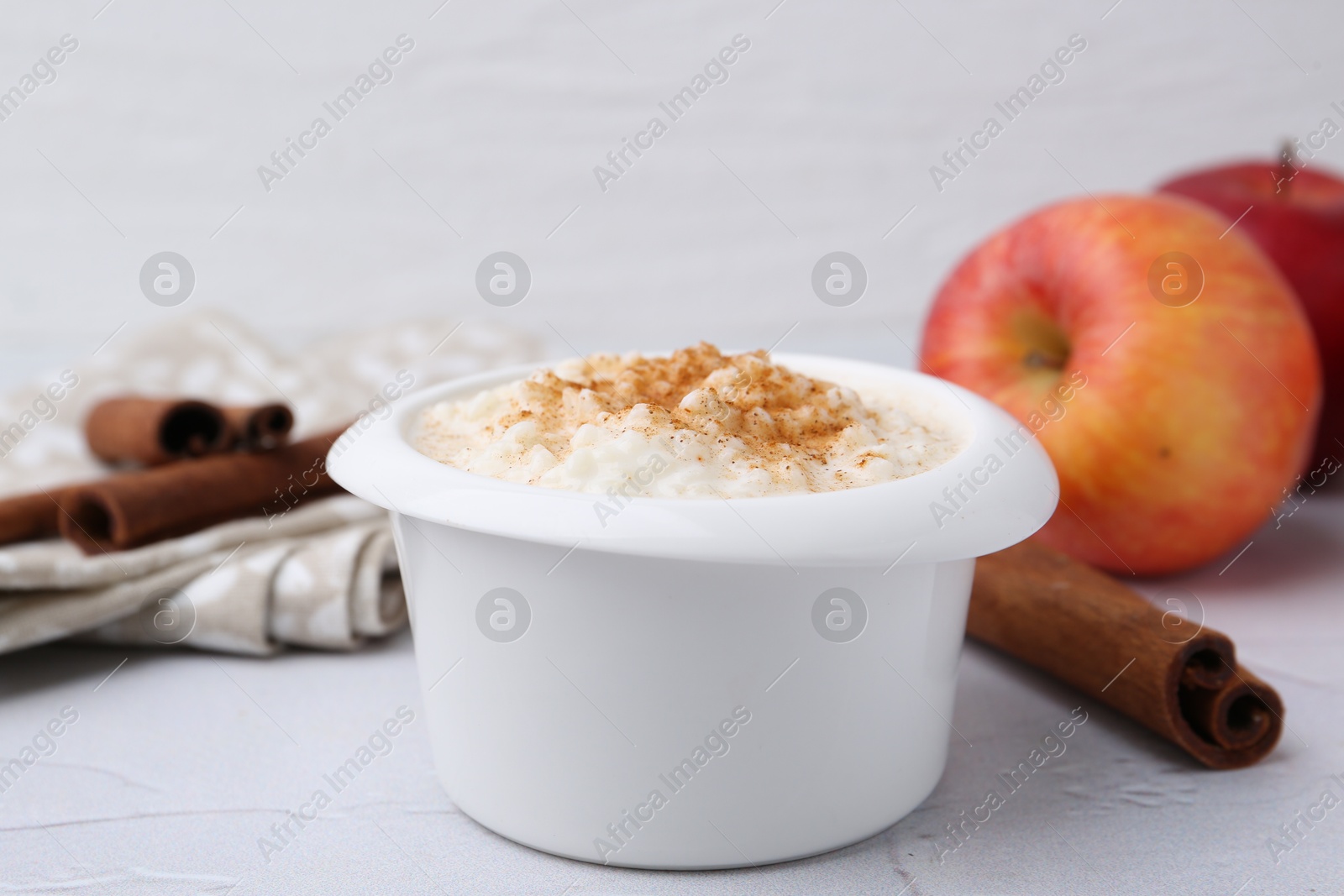 Photo of Delicious rice pudding with cinnamon and apples on white textured table, closeup