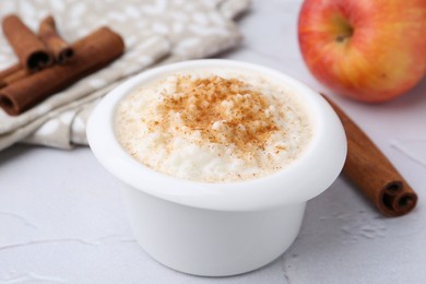 Photo of Delicious rice pudding with cinnamon and apple on white textured table, closeup