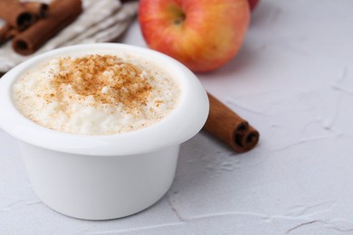 Photo of Delicious rice pudding with cinnamon and apple on white textured table, closeup. Space for text