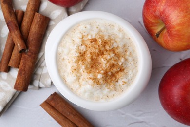 Photo of Delicious rice pudding with apples and cinnamon sticks on white textured table, flat lay