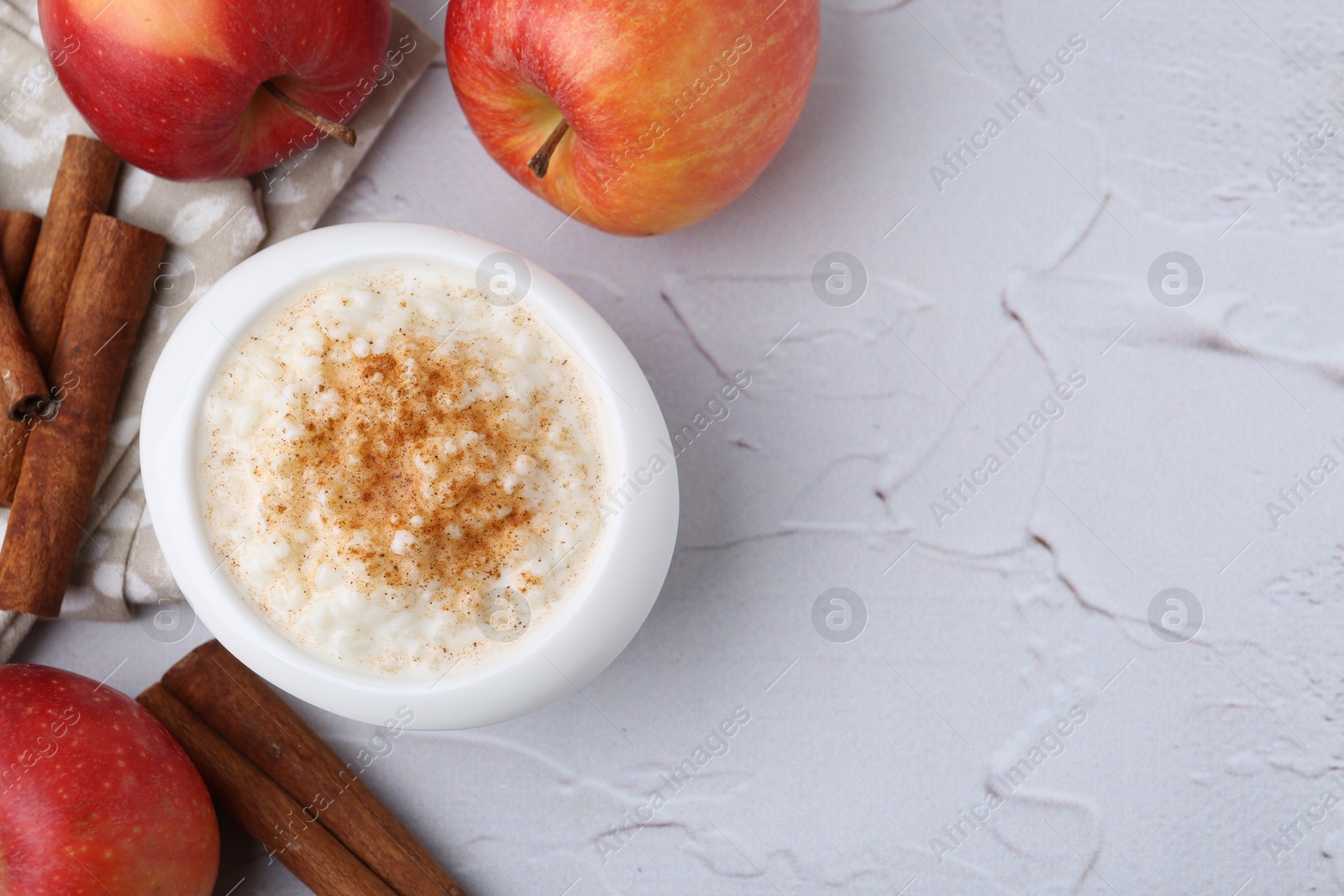 Photo of Delicious rice pudding with apples and cinnamon sticks on white textured table, flat lay. Space for text