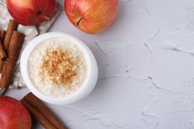 Photo of Delicious rice pudding with apples and cinnamon sticks on white textured table, flat lay. Space for text