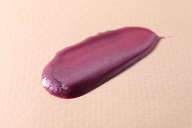 Photo of Sample of purple lipgloss on beige background, closeup