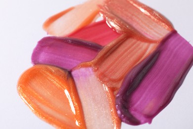 Photo of Samples of different lipglosses on light grey background, closeup