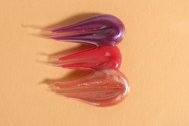 Photo of Samples of different lipglosses on beige background, top view