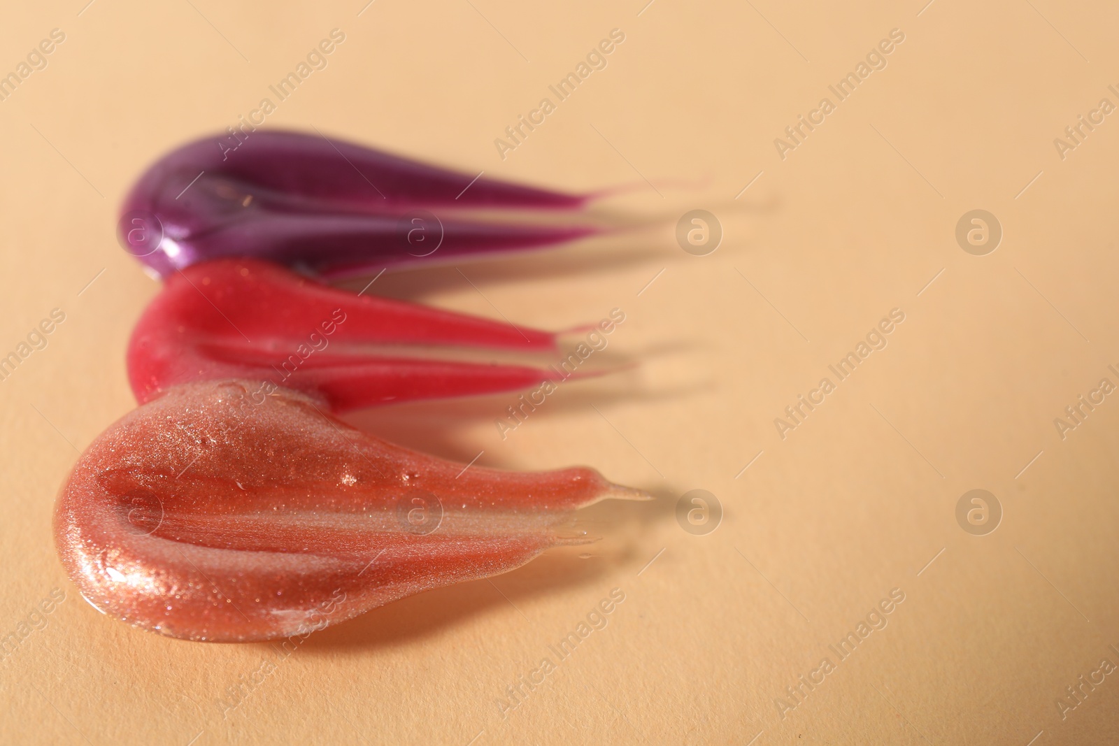 Photo of Samples of different lipglosses on beige background, closeup. Space for text