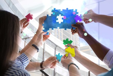 Image of People with puzzle pieces at office, closeup. Concept of partnership