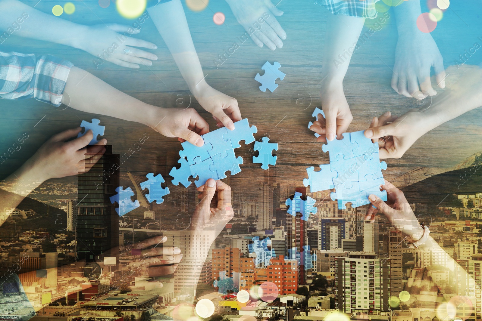 Image of People putting puzzle pieces together on wooden table, double exposure with cityscape. Concept of partnership