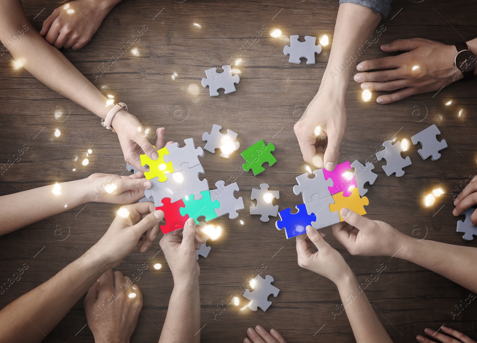 Image of People putting puzzle pieces together on wooden table, top view. Concept of partnership