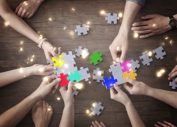 Image of People putting puzzle pieces together on wooden table, top view. Concept of partnership