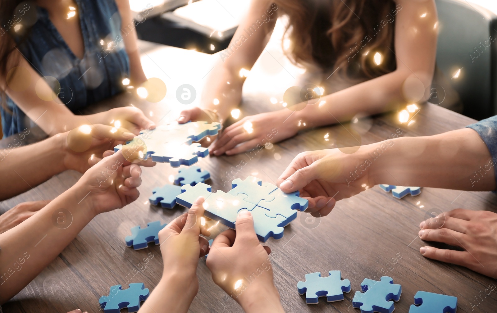 Image of People putting puzzle pieces together on wooden table, closeup. Concept of partnership