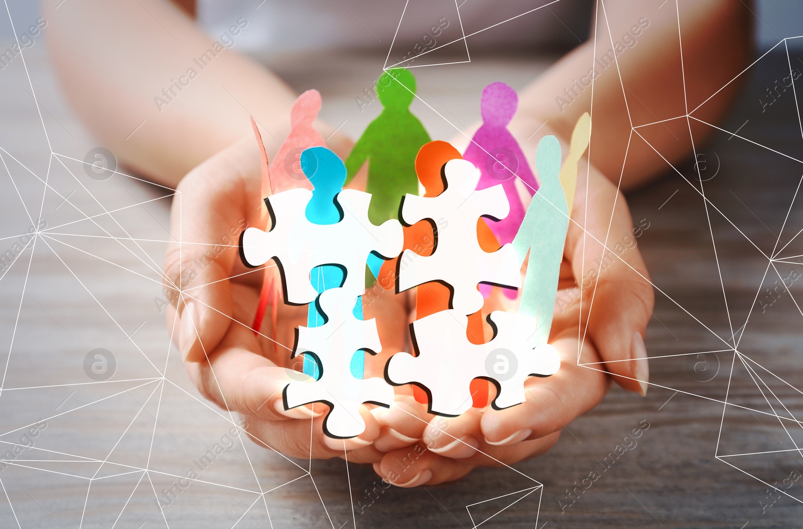 Image of Woman holding paper human figures at wooden table, double exposure with puzzle pieces. Concept of partnership