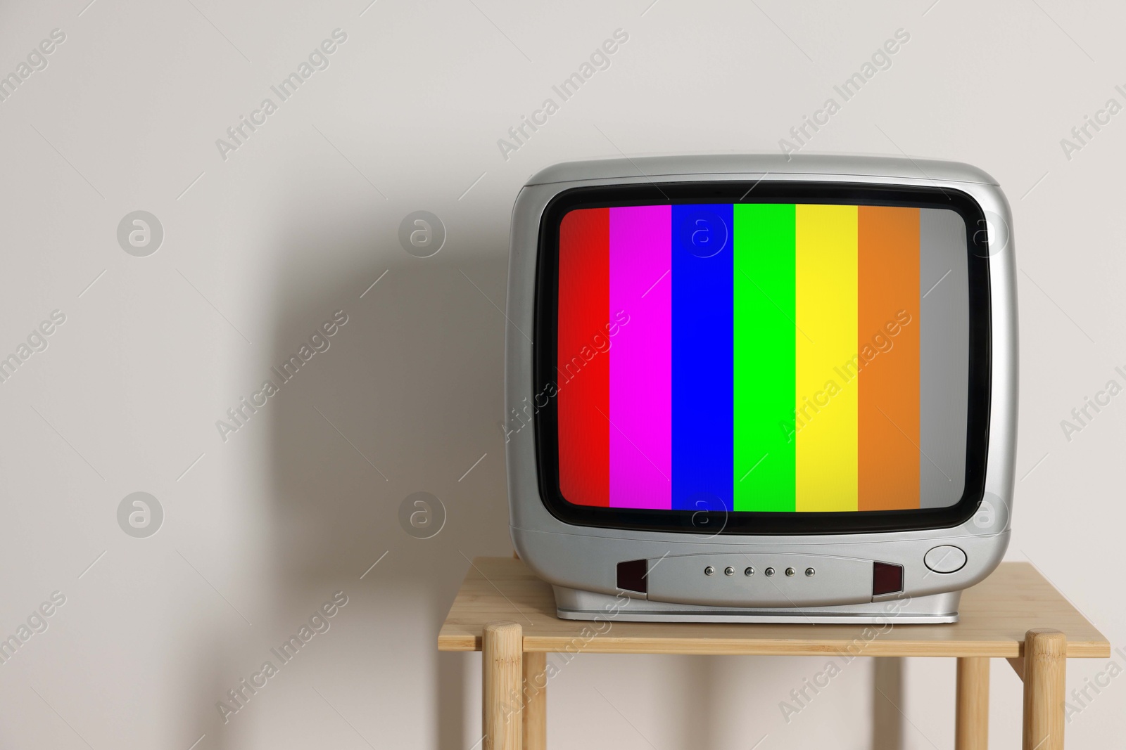 Image of Retro TV set with test pattern on wooden table near white wall. Color bars on screen. No signal