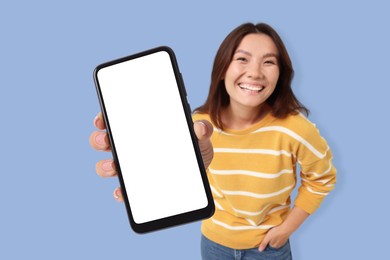 Image of Happy woman showing mobile phone with blank screen against pale blue background