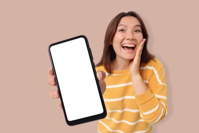 Surprised woman showing mobile phone with blank screen against dark beige background