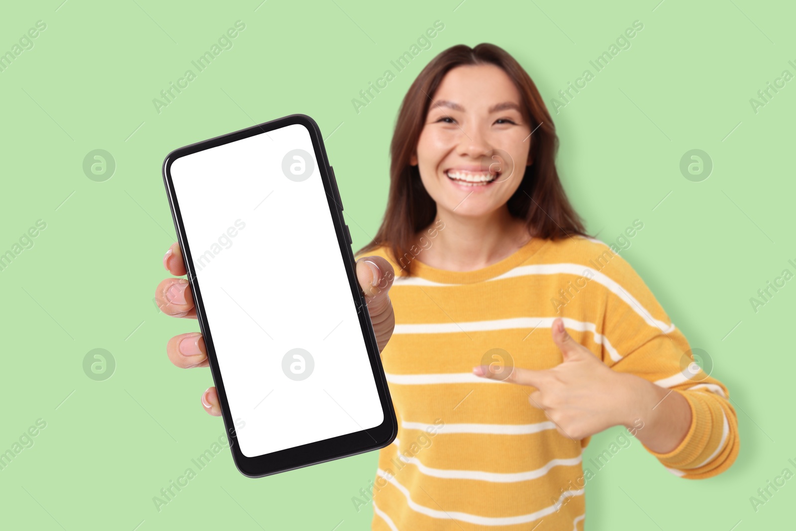 Image of Happy woman pointing at mobile phone with blank screen against light green background