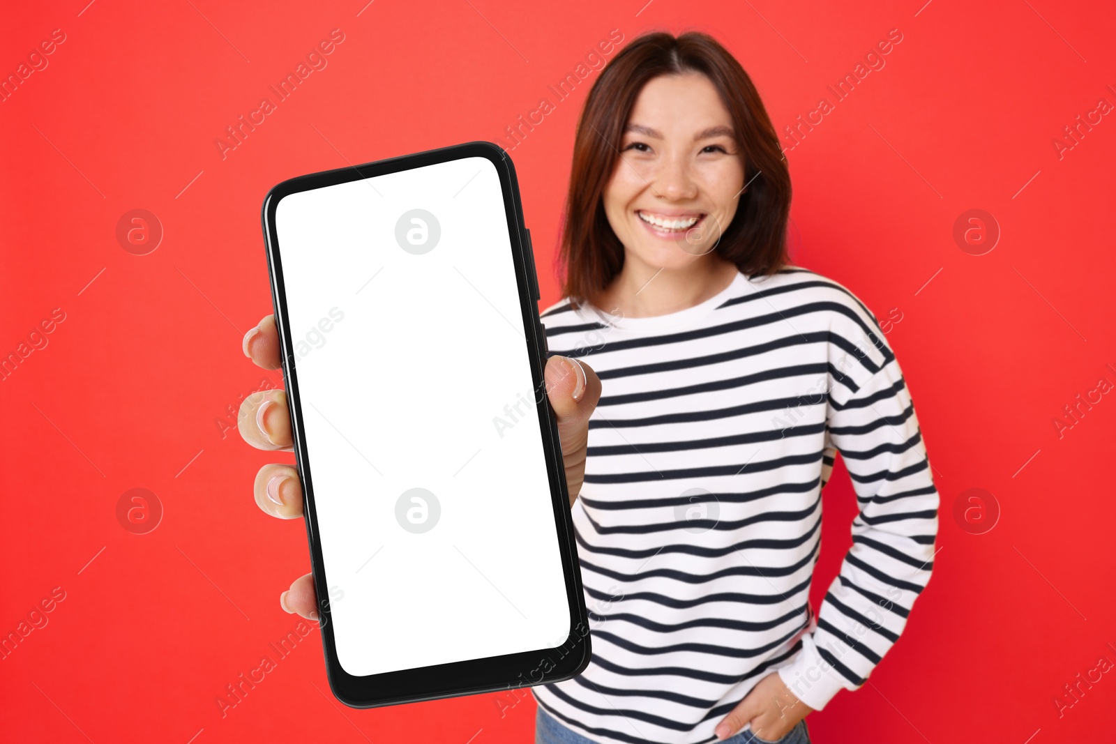 Image of Happy woman showing mobile phone with blank screen against red background