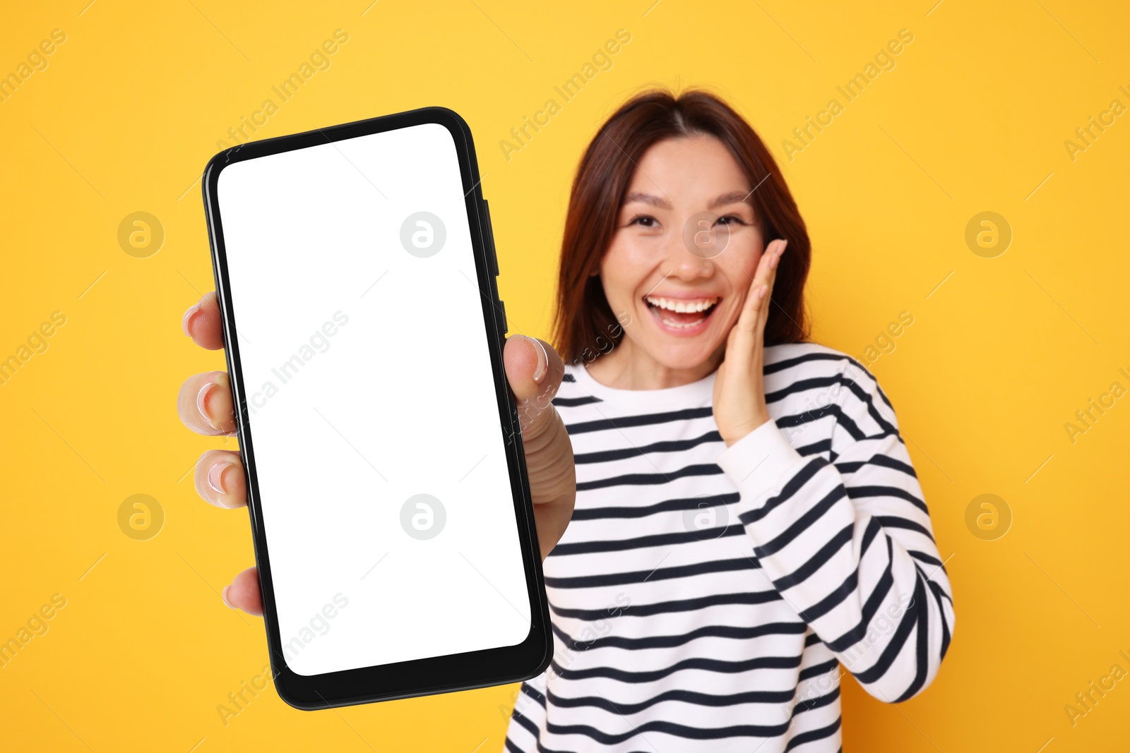 Image of Surprised woman showing mobile phone with blank screen against orange background