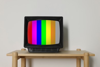 Image of Retro TV set with test pattern on wooden table near white wall. Color bars on screen. No signal