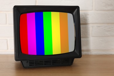 Image of Retro TV set with test pattern on wooden table near white brick wall. Color bars on screen. No signal