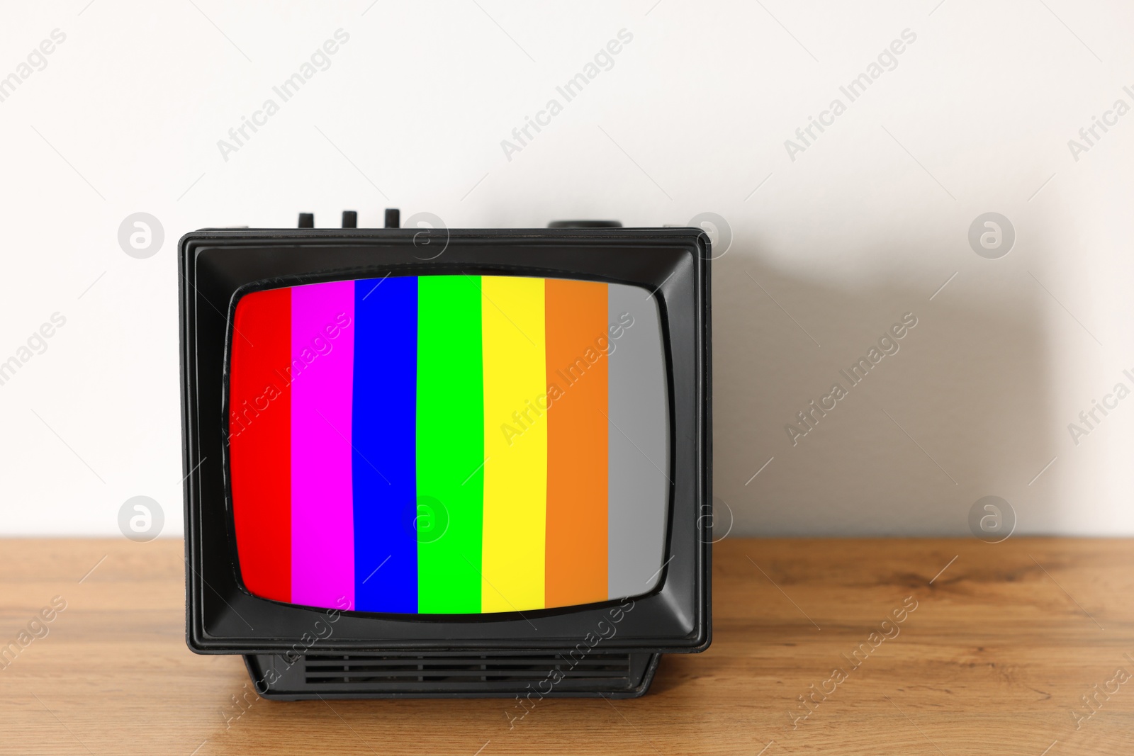 Image of Retro TV set with test pattern on wooden table near white wall. Color bars on screen. No signal