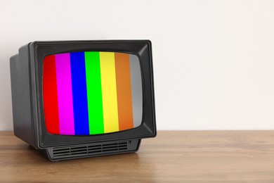 Image of Retro TV set with test pattern on wooden table near white wall. Color bars on screen. No signal