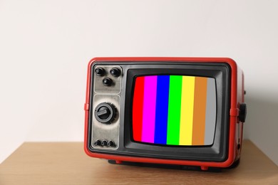 Image of Retro TV set with test pattern on wooden table near white wall. Color bars on screen. No signal