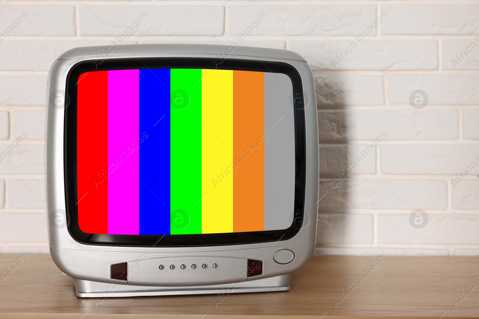 Image of Retro TV set with test pattern on wooden table near white brick wall. Color bars on screen. No signal