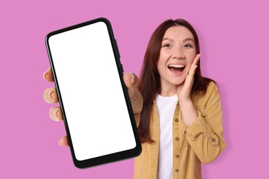 Surprised woman showing mobile phone with blank screen against pink background