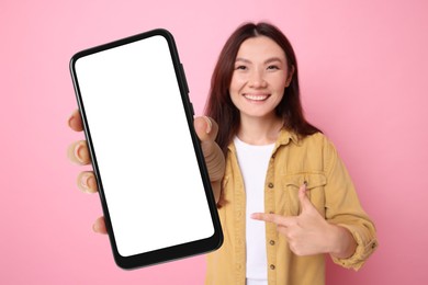 Image of Happy woman pointing at mobile phone with blank screen against pink background