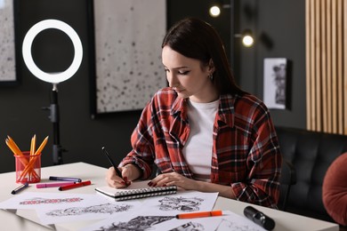 Photo of Tattoo artist drawing sketch with pen at white table in salon