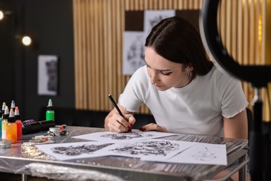 Photo of Tattoo artist drawing sketch at table with supplies in salon