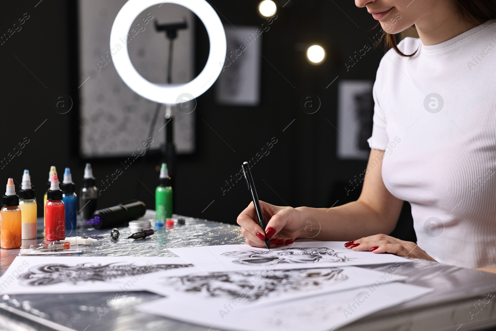 Photo of Tattoo artist drawing sketch at table with supplies in salon, closeup